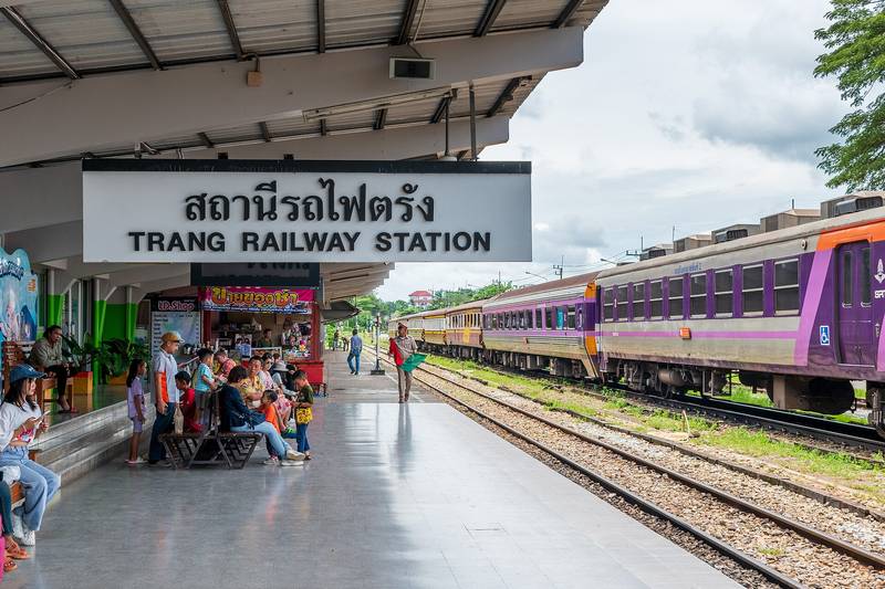 ชานชาลามีป้ายสถานีรถไฟตรัง ผู้โดยสารนั่งรอ และขบวนรถจอดอยู่ข้างราง